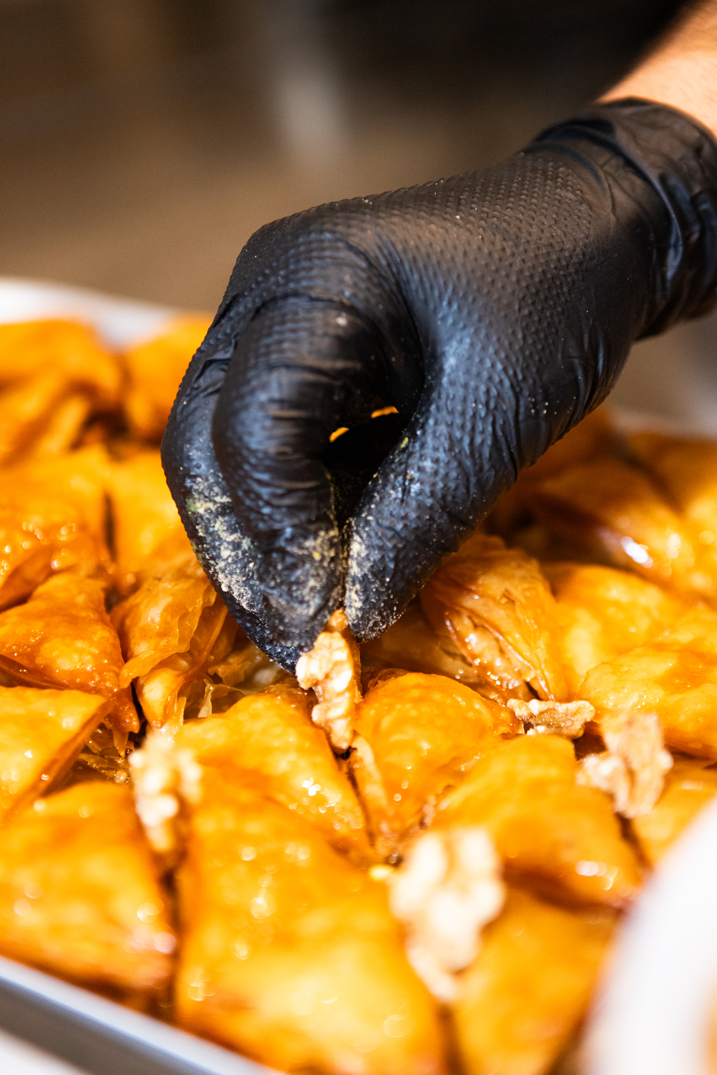 A baker's gloved hand plating fresh baklava on a tray at Adore Bakery