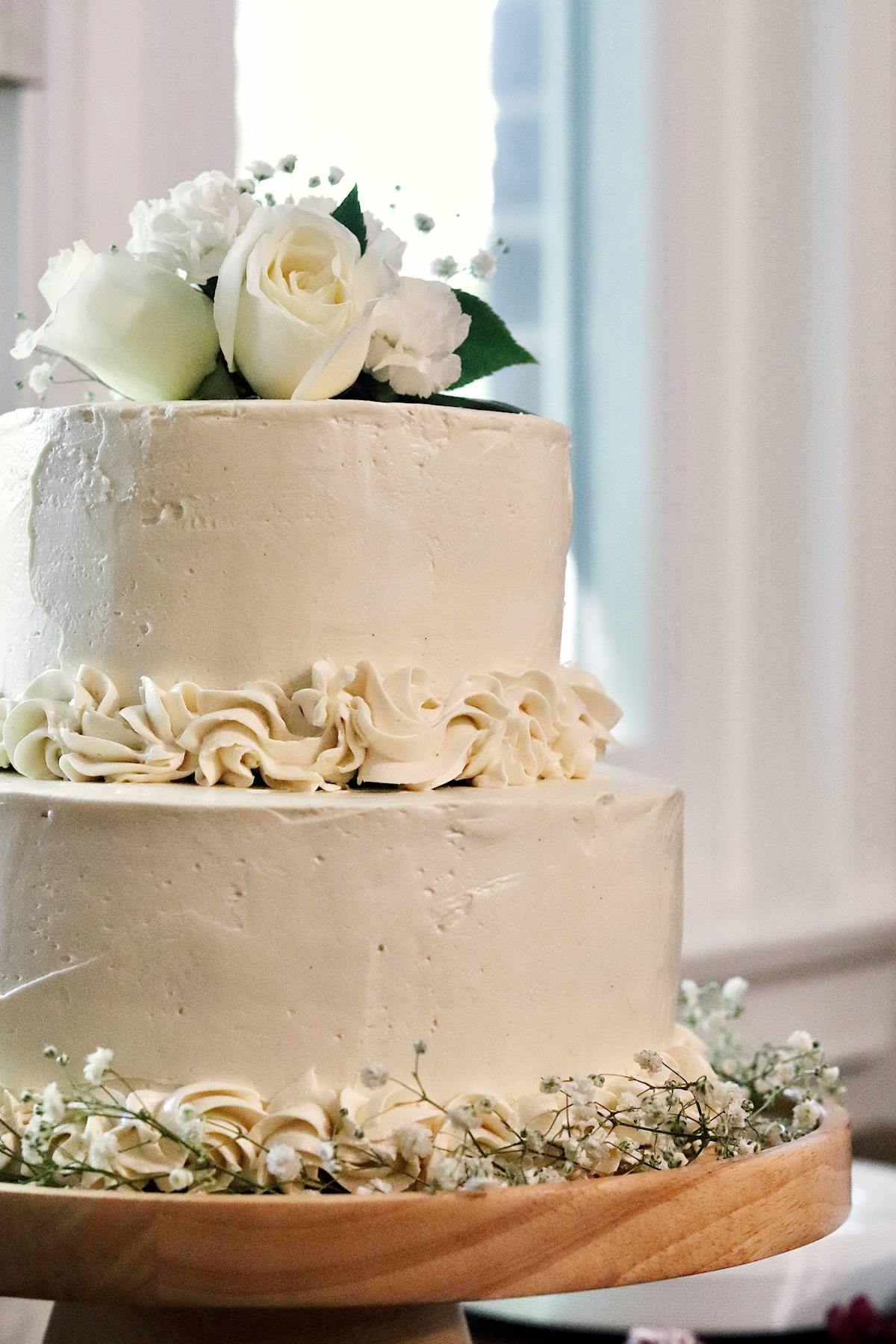 A two-tier white buttercream wedding cake topped with ivory roses and gypsophila