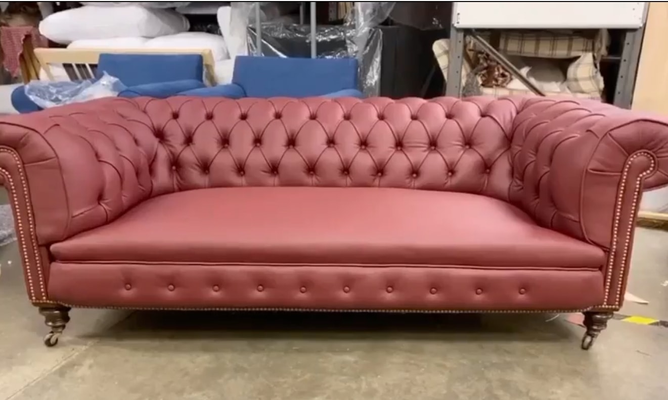 A fully-restored pink leather Chesterfield sofa — button-tufted, stud-detailed, on dark turned legs with brass castors, just out of the workshop