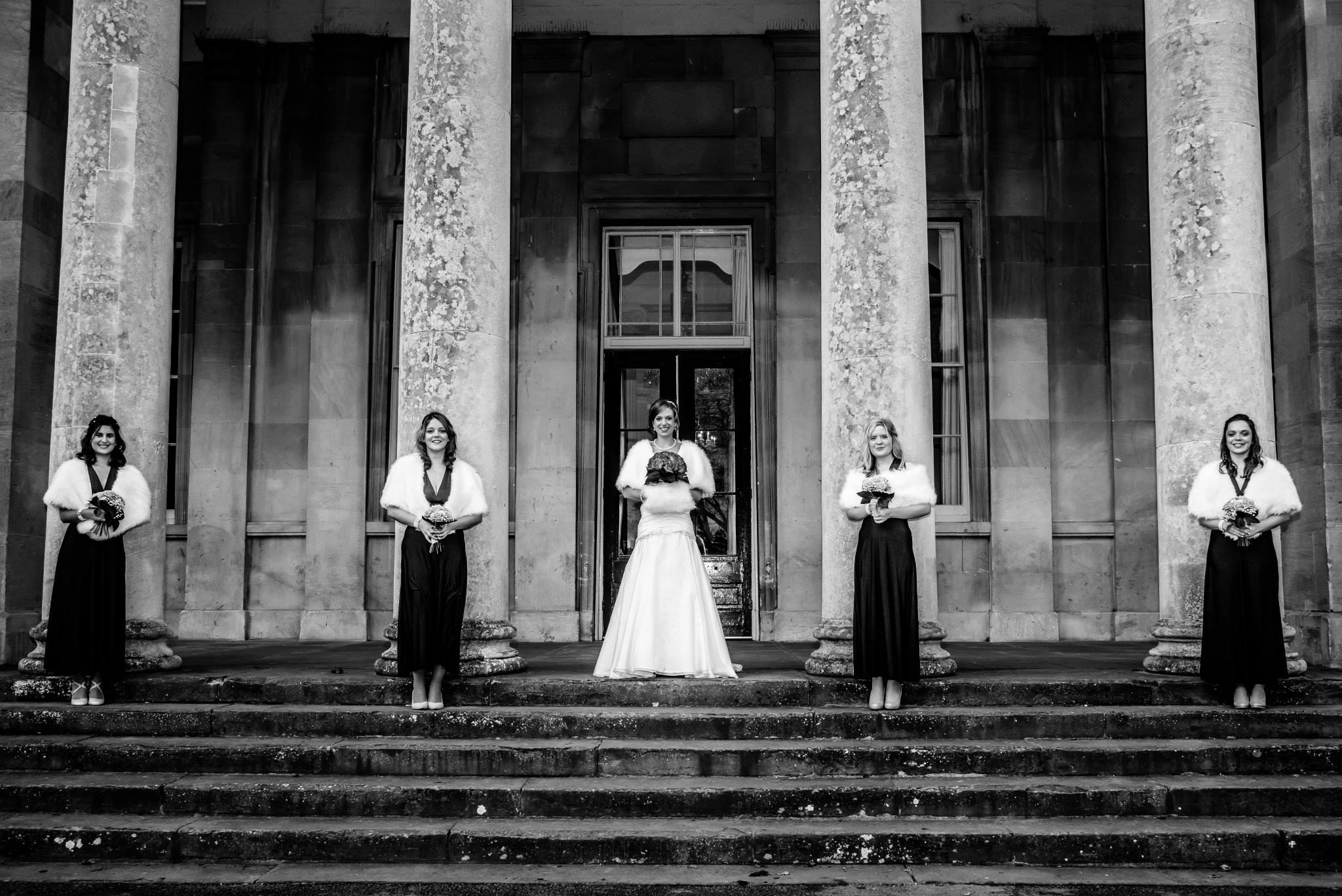Black-and-white bridal party photographed under stone columns at a Cotswold venue