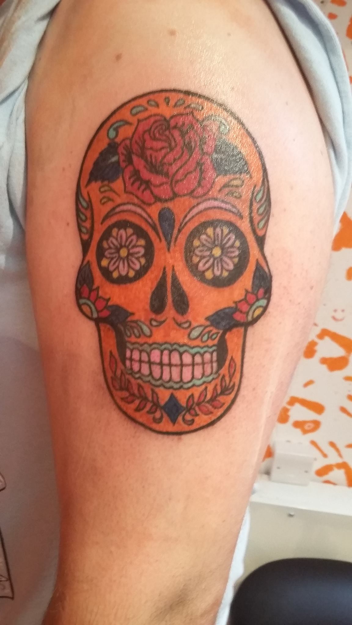 A sugar-skull tattoo, ornately detailed in black and grey with shading and pattern work