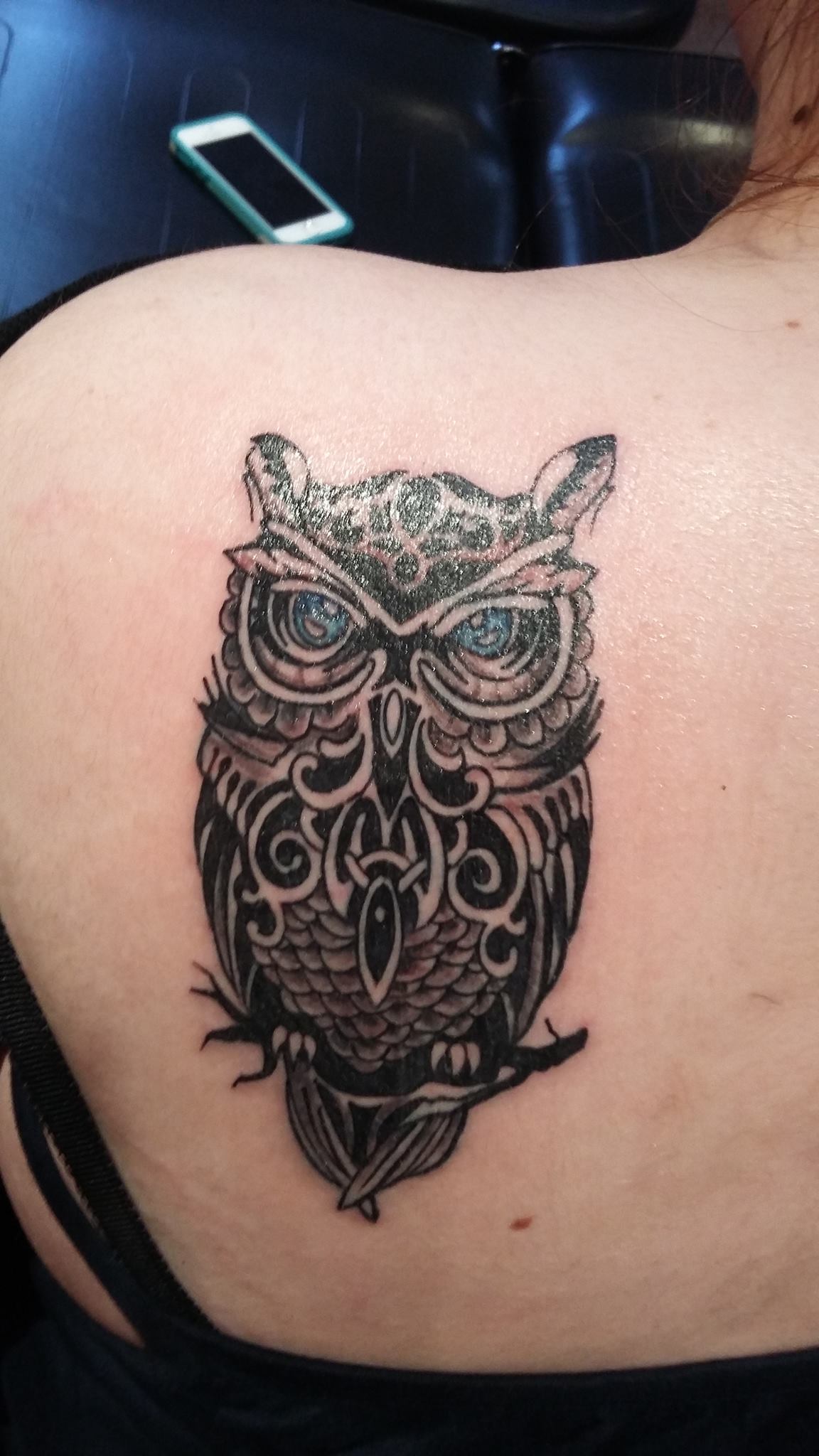 A black-and-grey ornate owl tattoo with tribal detailing across the upper back