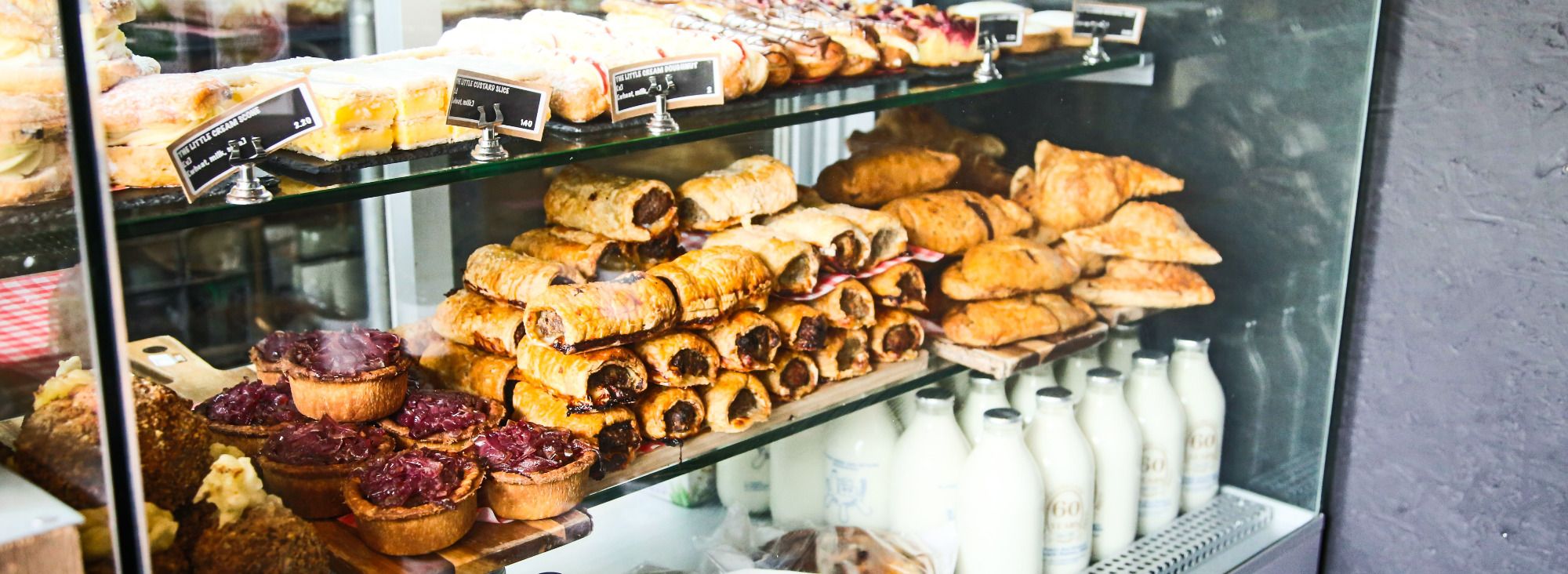 The Little Welsh Bakery counter — pastries, sausage rolls, fruit tarts and glass milk bottles behind the glass